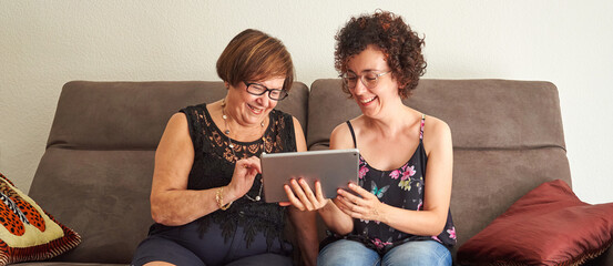Older woman and daughter share tablet while viewing family photos