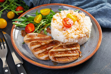 Rice with grilled pork meat, tomatoes and green herbs on dark background