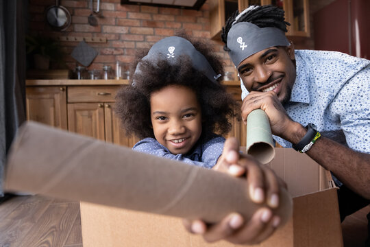 Portrait Of Overjoyed Young African American Dad And Teen Daughter Play Pirates In Ship Together At Home. Smiling Loving Ethnic Father And Small Girl Child Have Fun Involved In Playful Game Activity.