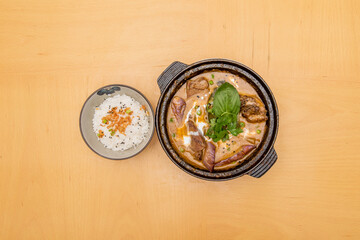 Top view image of red curry chicken stew with white rice and crispy onion on wooden table