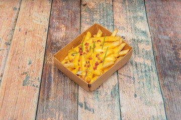 serving of crisps with diced pork bacon, lots of melted cheddar cheese and chopped chives in a cardboard home delivery container