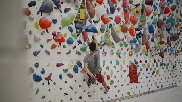 A rock climber guy trains on a special tena in the gym. Practicing rock climbing techniques