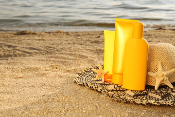 Sun protection products, hat and starfishes on sand near sea, space for text