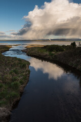 clouds reflected in a stream leading into the sea