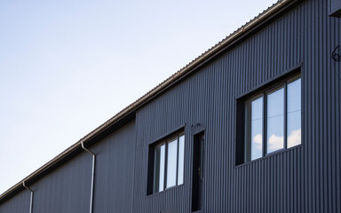 Black corrugated iron sheet used as a facade of a warehouse or factory with a windows. Texture of a seamless corrugated zinc sheet metal aluminum facade. Architecture. Metal texture.