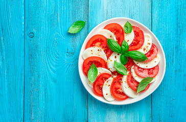 Caprese salad with fresh tomatoes, mozzarella cheese and basil leaves on a blue background.