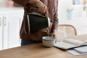 Close up crop of ethnic female student make coffee feel exhausted studying preparing for exam at...
