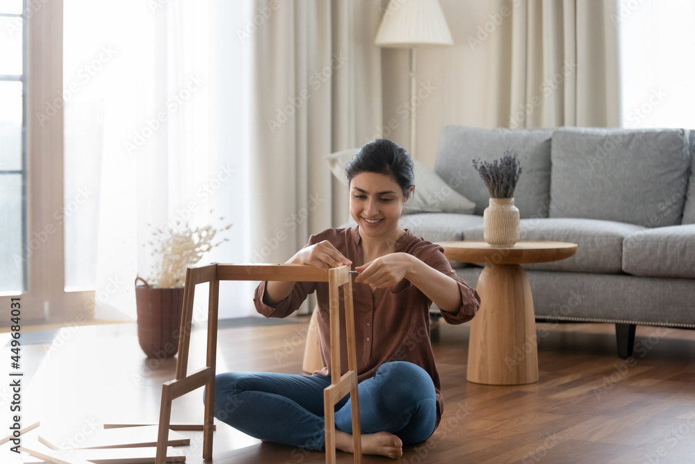 Wall mural happy millennial indian female renter or tenant sit on floor in new house gather shelf. smiling youn