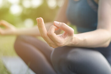 Photo of an unrecognizable woman meditating in the park. Woman in lotus position in nature, close-up. Meditation and relaxation