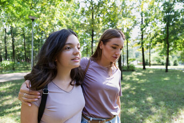 Fototapeta premium Mom and teenage daughter take a walk in the summer park. Using a smartphone