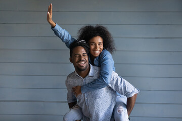 Overjoyed young African American couple renters have fun hug cuddle isolated on grey wall...