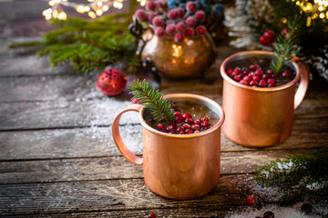 Mulled wine with cranberry in copper mug with christmas decorations on wooden table