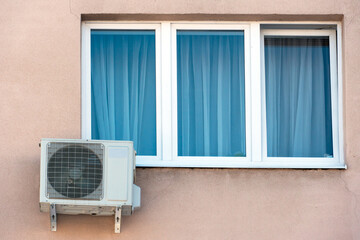 An outdoor air conditioner unit installed on the wall of a residential building next to the window. Installation, repair and maintenance of air conditioning systems in residential premises.