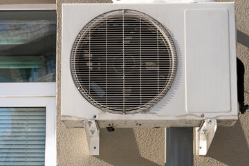 An outdoor air conditioner unit installed on the outer wall of a residential building close-up. Operation of the air conditioner in winter at low temperatures. Icicles and snow on the air conditioner