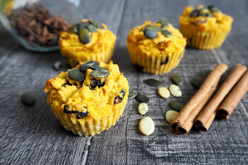 several gluten-free pumpkin muffins, sprinkled with pumpkin seeds, are lying on a wooden table next to cinnamon sticks . side view. vegan sweets