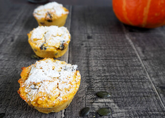 three gluten-free pumpkin muffins, sprinkled with powdered sugar, lie on a wooden table next to a pumpkin in the background . side view