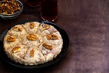 sunflower halva with fork and Turkish tea in traditional glass on the wooden table close-up. glass cup of black tea with walnuts on the dark brown background with copy space. Turkish desserts.