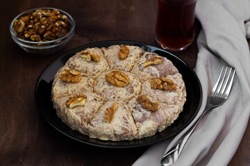 sunflower halva with fork and Turkish tea in traditional glass on the wooden table close-up. glass cup of black tea with walnuts on the dark brown background with copy space.