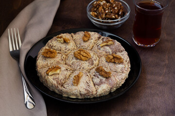 Turkish desserts. sunflower halva with fork and Turkish tea in traditional glass on the wooden table close-up. glass cup of black tea with walnuts on the dark brown background with copy space.