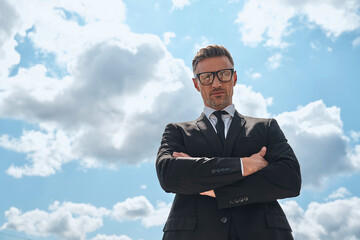 Low angle view of confident mature man in full suit keeping arms crossed