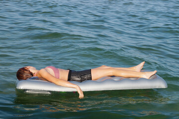 girl sunbathes on an inflatable mattress on the water
