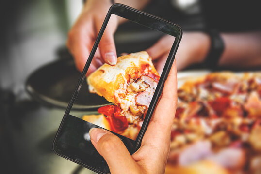 woman hand holding and showing smart phone takes a photo woman Hand takes a slice of meat Pizza with Mozzarella cheese, salami, Tomatoes, pepper, ham, Spices and chicken in cafe. food photos