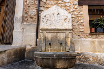 Old stone fountain adorned with masonry details, from which clear and crystalline water flows. 