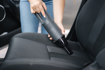 Close up of female using portable vacuum cleaner in her car. Electrical vacuum in woman's hand clean car inside from dust