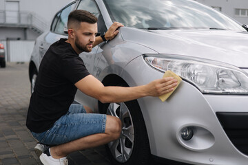 Fototapeta na wymiar Hand of man wipes headlight of his car using rug. Self-service car wash. Outdoor
