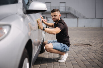 Handsome man wipes a car with a rag in a showroom at a self-service car wash. Gray car