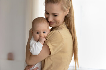Happy young Caucasian mom hold in arms hug caress little newborn son or daughter play with kid child. Smiling mother embrace lull small baby infant show love care. Motherhood concept.
