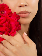 Macro photo of female lips with beautiful skin and nude makeup. light transparent gloss on full lips and red flowers. Fashion photography. Cosmetology and spa. Freshness of spring
