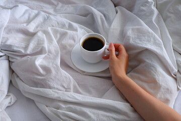 Girl holding a cup of coffee in bed. Breakfast in bed. Interior. Cosiness.