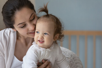 Close up of smiling young Caucasian mother play with cute small newborn baby kid child at home. Happy loving caring mom relax caress cuddle little infant daughter. Motherhood, parenthood concept.