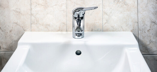 Chromed faucet with lever to mix hot and cold water on a modern white sink in a bathroo