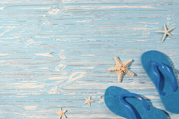 Sea stars and rubber beach blue flip flops on blue wooden background