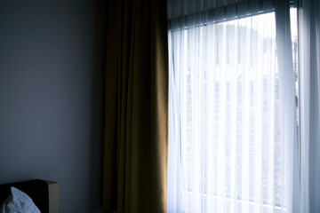 corner of hotel bedroom with white curtain in front of window