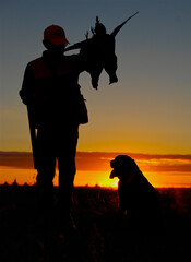 Hunter with pheasant and dog at sunset 