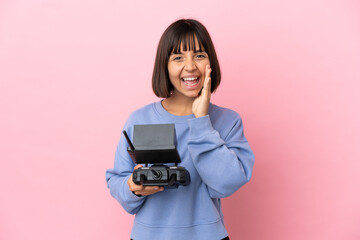 Young mixed race woman holding a drone remote control isolated on pink background shouting with mouth wide open