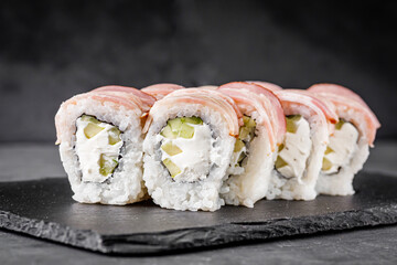 appetizing sushi roll with philadelphia cheese cucumber and bacon on a black stone plate