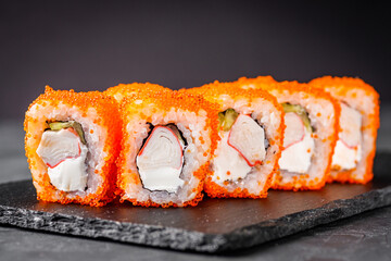 appetizing sushi roll california with cheese cucumber crab and masago caviar on a black stone plate