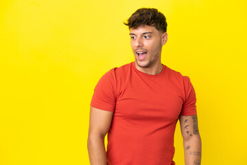 Young caucasian handsome man isolated on yellow background doing surprise gesture while looking to the side