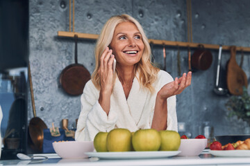 Beautiful mature woman in bathrobes talking on mobile phone and smiling