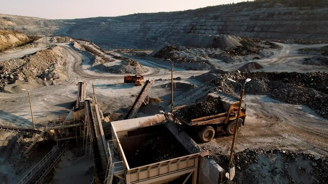 Quarry dump truck unloads the rock into a rock crusher. Open pit mine quarrying extractive industry stripping work. Big Yellow Mining Trucks
