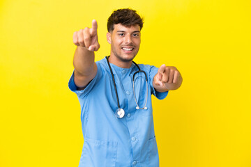 Fototapeta premium Young surgeon doctor man isolated on yellow background points finger at you while smiling