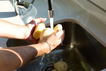 Man washing potatoes in the sink, no faces shown