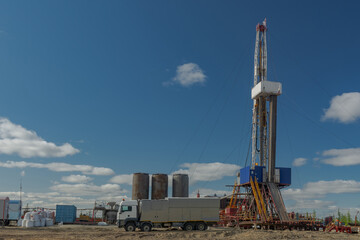The drilling rig is included in the landscape of the oil and gas field. Infrastructure, communications and drilling equipment are visible. The drilling rig has equipment for well cementing