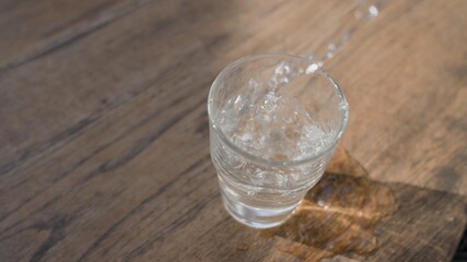 After the party, a person pours water into a glass but from shaking hands spills water past the glass directly on the table. Vodka is poured into a faceted glass. Water pours past a glass.
