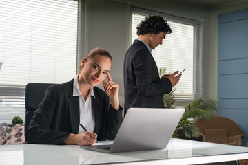 Smiling businesswoman sitting at the desk in front of laptop, businessman using smartphone office background. Concept of teamwork