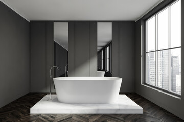 Grey bathroom with dark parquet flooring, a white bathtub and marble platform